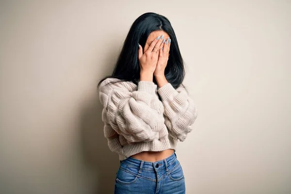Young beautiful chinese woman wearing casual sweater over isolated white background with sad expression covering face with hands while crying. Depression concept.