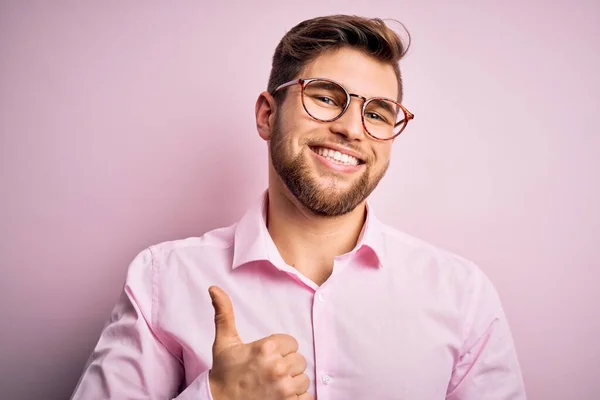 年轻英俊的金发男人 留着胡子 蓝眼睛 穿着粉色衬衫 戴着眼镜 手拿着快乐的大拇指 在镜头前看着成功的表情 — 图库照片