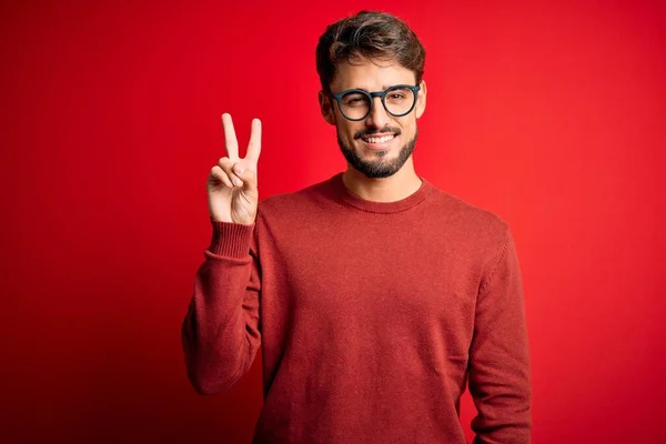 Sakallı Gözlüklü Süveterli Genç Adam Kırmızı Arka Planda Dikiliyor Parmaklarıyla — Stok fotoğraf