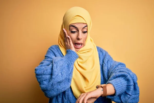 年轻美丽的黑发穆斯林女子 头戴阿拉伯头巾 头戴黄褐色的背景 看着钟表 忧心忡忡 生怕迟到 — 图库照片