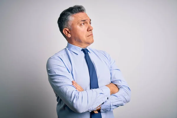 Middle age handsome grey-haired business man wearing elegant shirt and tie looking to the side with arms crossed convinced and confident