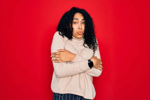 Young african american curly woman wearing casual turtleneck sweater over red background shaking and freezing for winter cold with sad and shock expression on face