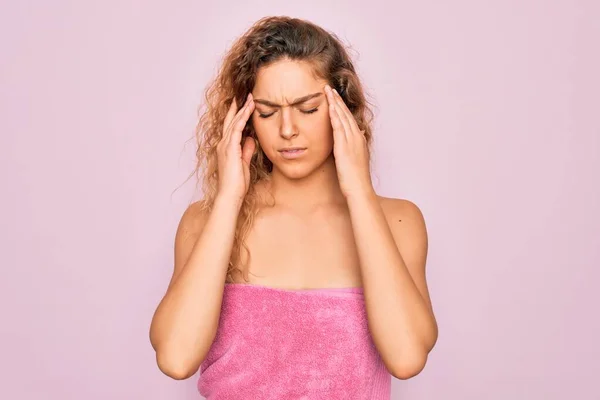 stock image Beautiful blonde woman with blue eyes wearing towel shower after bath over pink background with hand on head for pain in head because stress. Suffering migraine.