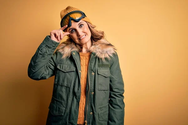 中年漂亮的金发滑雪者女人穿着雪地运动鞋和滑雪护目镜 担心并强调了一个手握额头 紧张和焦虑的问题 — 图库照片