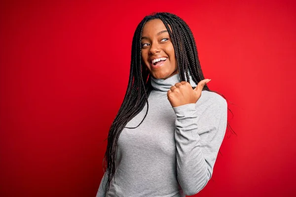 若いですアフリカ系アメリカ人女性身に着けていますTurtleeckセーター以上赤隔離された背景笑顔で幸せな顔見ますとポインティングで側面に親指アップ — ストック写真