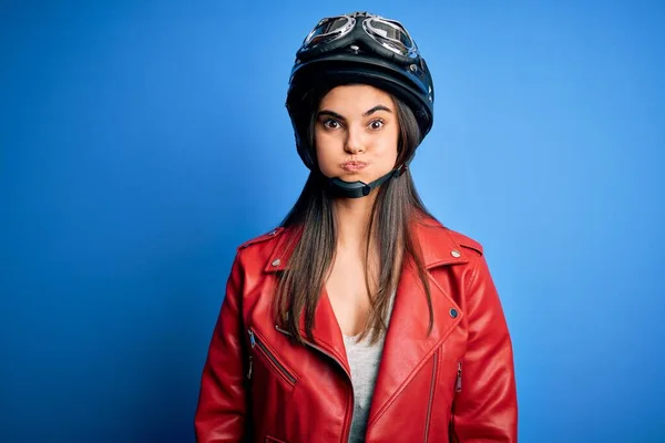 若い美しいブルネットのオートバイのヘルメットとジャケットを身に着けている女性は面白い顔で頬をパフ 口は空気で膨脹し 狂気の表現 — ストック写真