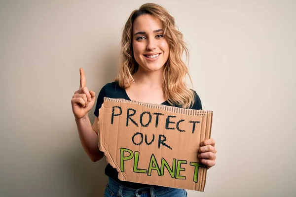 Young activist woman asking for environment holding banner with protect planet message surprised with an idea or question pointing finger with happy face, number one