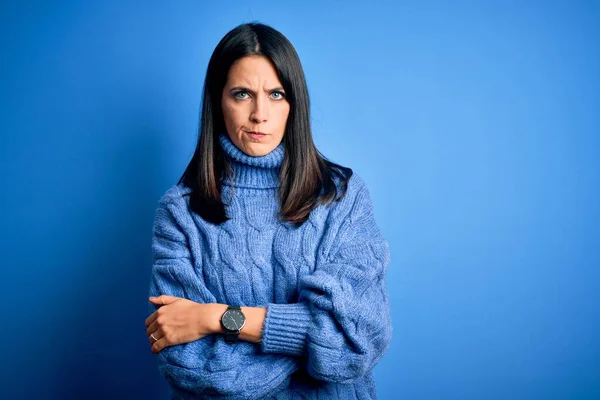 Young brunette woman with blue eyes wearing casual turtleneck sweater skeptic and nervous, disapproving expression on face with crossed arms. Negative person.