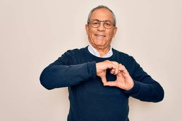 Senior handsome grey-haired man wearing sweater and glasses over isolated white background smiling in love doing heart symbol shape with hands. Romantic concept.