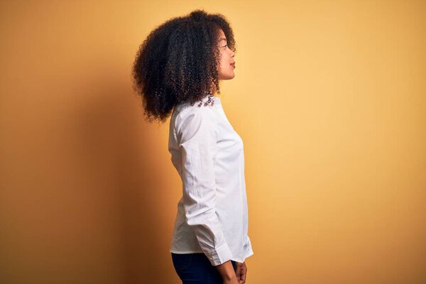 Young beautiful african american elegant woman with afro hair standing over yellow background looking to side, relax profile pose with natural face and confident smile.