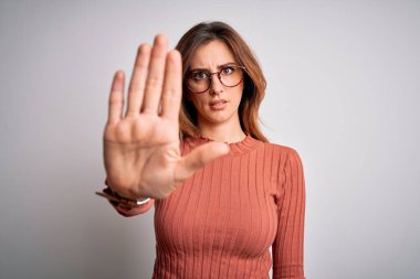 Genç, güzel, esmer bir kadın beyaz arka planda günlük süveter ve gözlük takıyor ve avuç içiyle şarkı söylemeyi kesiyor. Yüzünde olumsuz ve ciddi bir jest olan uyarı ifadesi.