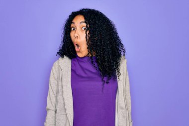 Genç Afro-Amerikan sporcu kadın mor arka plan üzerine günlük kazak giyiyor korku, korku ve heyecan dolu yüz ifadesinden korkuyor ve şoka uğruyor..