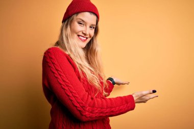 Beyaz arka plan üzerine yün başlık takmış genç, güzel sarışın kadın gülümseyerek içeri girmeye davet ediyor.