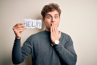 Kıvırcık saçlı genç bir adam beyaz arka plan üzerinde yardım mesajı taşıyan bir kağıt tutuyordu. Ağzı, hata yüzünden utançla kaplıydı. Korkunun ifadesi, sessizlikten korkmak, gizli bir konsept.