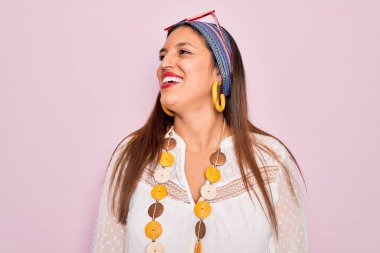 Genç İspanyol hippi kadın pembe arka planda boho tarzı ve güneş gözlüğü takıyor. Yüzünde gülümseme, doğal bir ifade ile diğer tarafa bakıyor. Kendinden emin gülen.