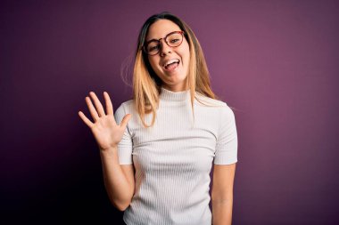 Mor arka planda mavi tişörtlü, mavi gözlü genç, güzel sarışın kadın beş numarayı gösterirken kendinden emin ve mutlu bir şekilde gülümsüyor..