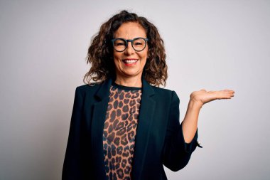 Orta yaşlı esmer iş kadını gözlüklü, izole edilmiş beyaz arka planda duran neşeli bir şekilde gülümseyen ve avuç içi kameraya bakan..