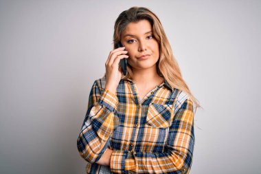 Güzel sarışın kadın, beyaz arka planda akıllı telefondan konuşuyor. Akıllı yüzünde kendine güvenen bir ifade var. Ciddi düşünüyor.