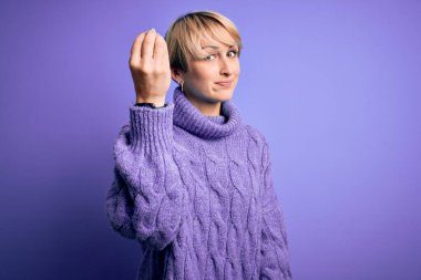 Sarışın, kısa saçlı, mor arka planda balıkçı yaka kazak giyen, el ve parmak hareketleriyle İtalyanca konuşan, kendine güvenen bir kadın.