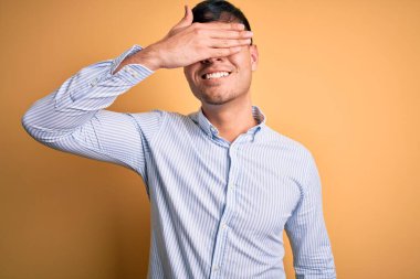 Sarı arka planda inek gözlüğü takan genç, yakışıklı İspanyol iş adamı. Gülümsüyor ve yüzünde şaşkınlıktan gözleri kapayarak gülüyor. Kör kavram.