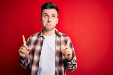 Kırmızı izole arka plan üzerine gündelik modern gömlek giyen genç beyaz adam üzgün ve üzgün görünüyor, parmaklarıyla yönü gösteriyor, mutsuz ve depresif..
