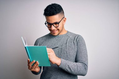 Genç, yakışıklı, zeki bir öğrenci, izole beyaz arka planda kitap okuyor. Mutlu bir yüzü var, gülümsüyor ve kendine güvenen bir gülümsemeyle dişlerini gösteriyor.