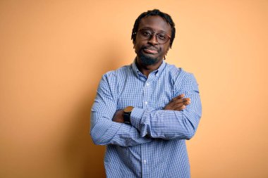 Sarı arka plan üzerine gömlek ve gözlük takan yakışıklı afro-amerikalı genç adam şüpheci ve gergin, yüzünde çapraz kollu tasvip etmeyen bir ifade. Negatif kişi.