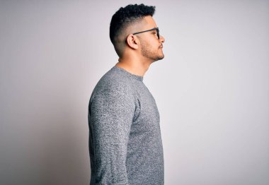 İzole edilmiş beyaz arkaplanda gözlük takan genç yakışıklı bir adam yan tarafa bakıyor, rahat bir görünüm sergiliyor kendine güvenen bir gülümsemeyle doğal bir yüze sahip..