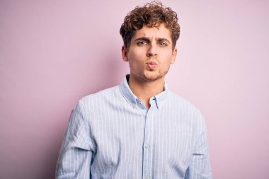 Sarışın, kıvırcık saçlı, beyaz arka planda çizgili tişört giyen, güzel ve seksi bir şekilde havada öpüşen kameraya bakan genç bir adam. Aşk ifadesi.