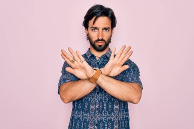 Genç, yakışıklı, bohem, pembe arka planda hippi tarzı giyinmiş, reddedilmiş, kollarını kavuşturmuş, negatif işaretler veren, kızgın yüzlü bir adam.