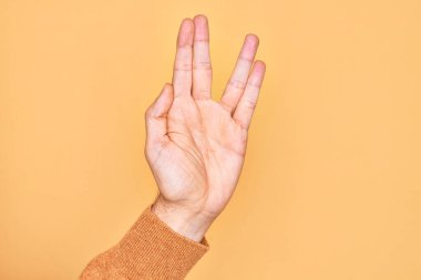 Kafkasyalı genç adam parmaklarını izole edilmiş sarı arka planda gösteriyor. Vulkan selamı veriyor, el ve parmaklarını gösteriyor, ucube kültürü sergiliyor.