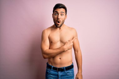 Sakalsız, genç, yakışıklı, güçlü bir adam pembe arka planda dikiliyor. Parmakla işaret ediyor, ağzı açık, şaşkın bir ifade..