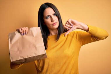 Mavi gözlü genç esmer kadın elinde kızgın yüzlü yemek torbası, olumsuz işaret baş parmakları aşağıda, reddedilme konsepti var.