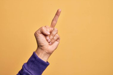 Hand of caucasian young man showing fingers over isolated yellow background showing provocative and rude gesture doing fuck you symbol with middle finger