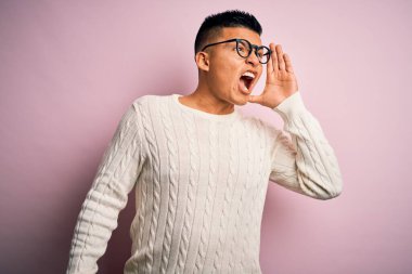 Beyaz süveter giyen, pembe arka planda gözlük takan genç, yakışıklı Latin bir adam el ele verip bağırıyor. İletişim konsepti.