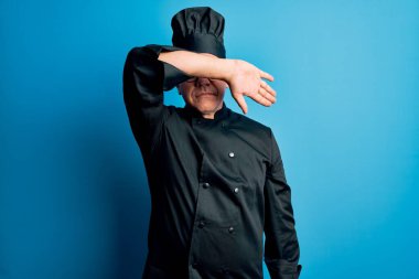 Orta yaşlı, yakışıklı, gri saçlı aşçı fırın üniforması giyen ve şapkasını kollarıyla kapatan, ciddi ve üzgün görünen bir adam. Görme, saklama ve reddetme konsepti