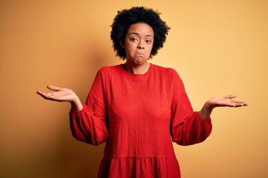 Kıvırcık saçlı, sıradan bir süveter giyen, elleri ve kolları havada, kafası karışmış genç ve güzel Afro-Amerikan bir kadın. Şüphe kavramı.