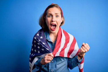 Birleşik Devletler bayrağını takan genç, güzel sarışın kadın mavi arka planda gururla bağırıyor ve zaferi ve başarıyı kutluyor. Çok heyecanlı, coşkulu bir duygu.