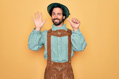Almanya Festivali için geleneksel Alman Ekim Festivali kıyafeti giyen genç yakışıklı adam altı numarayı gösterip işaret ederken kendinden emin ve mutlu bir şekilde gülümsüyor..