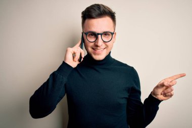 Yakışıklı, beyaz bir adam akıllı telefondan konuşuyor. Elini ve parmağını yana uzatarak mutlu bir şekilde konuşuyor.