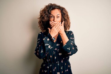 İzole edilmiş beyaz arka planda dikilen gündelik elbise giyen orta yaşlı güzel bir kadın yanlışlıkla ağızlarını kapatarak şok geçirdi. Gizli konsept.