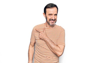 Orta yaşlı, çizgili tişört giyen yakışıklı adam izole edilmiş beyaz arka planda dikiliyor. Gülümsüyor, eli ve parmağı yana doğru uzanıyor.