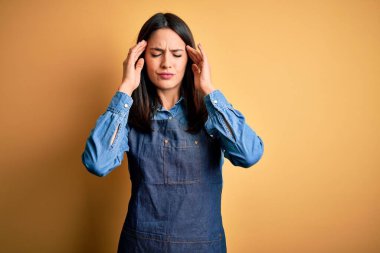 Mavi gözlü genç fırıncı kadın izole edilmiş sarı arka planda dikiliyordu. Ağrı ve migren yüzünden baş ağrısı ve stres yaşıyordu. Ellerini başının üstüne koy..