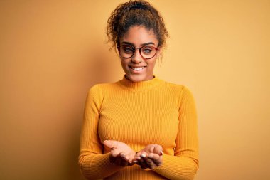 Sarı arka planda süveter ve gözlük takan güzel afro-amerikalı kız avuçlarını birbirine uzatarak gülümsüyor ya da el hareketi yapıyor. Tutun ve koruyun