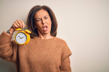 Orta yaşlı esmer kadın, arka planda izole edilmiş, klasik çalar saati elinde tutuyor. Şok suratlı, şüpheci, alaycı ve ağzı açık bir şekilde bakıyor.