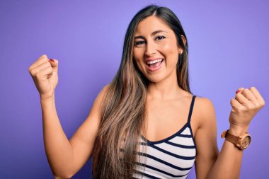 Mor izole edilmiş arka plan üzerine sıradan çizgili giyinen genç ve güzel bir kadın kollarını kaldırarak ve açık gözlerle başarıyı kutluyor ve şaşırıyor. Kazanan konsept.