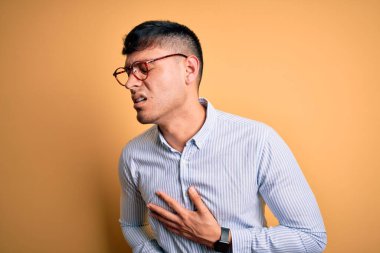 Yakışıklı İspanyol iş adamı sarı arka planda inek gözlüğü takıyor. Midesi bulanıyor ve acı çekiyor. Ache kavramı.