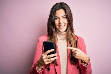 Genç ve güzel bir kız beyaz arka plan üzerinde akıllı telefon kullanarak sohbet ediyor. Elle ve parmakla işaret ederek çok mutlu.