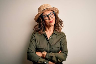 Orta yaşlı esmer kadın gözlüklü ve şapkalı izole edilmiş beyaz arka planda duruyor gülümsüyor ve uzaklara bakıyor..