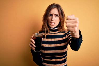 Genç, güzel esmer kadın, bardakla kola içerken pipet kullanıyor. Sinirli ve sinirlenmiş bir şekilde bağırıyor, çıldırıyor ve el kaldırarak bağırıyor. Öfke kavramı.